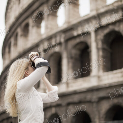 A woman outside the Colosseum amphitheatre in Rome, taking photographs.