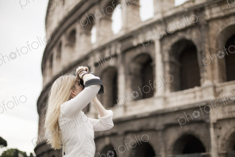 A woman outside the Colosseum amphitheatre in Rome, taking photographs.