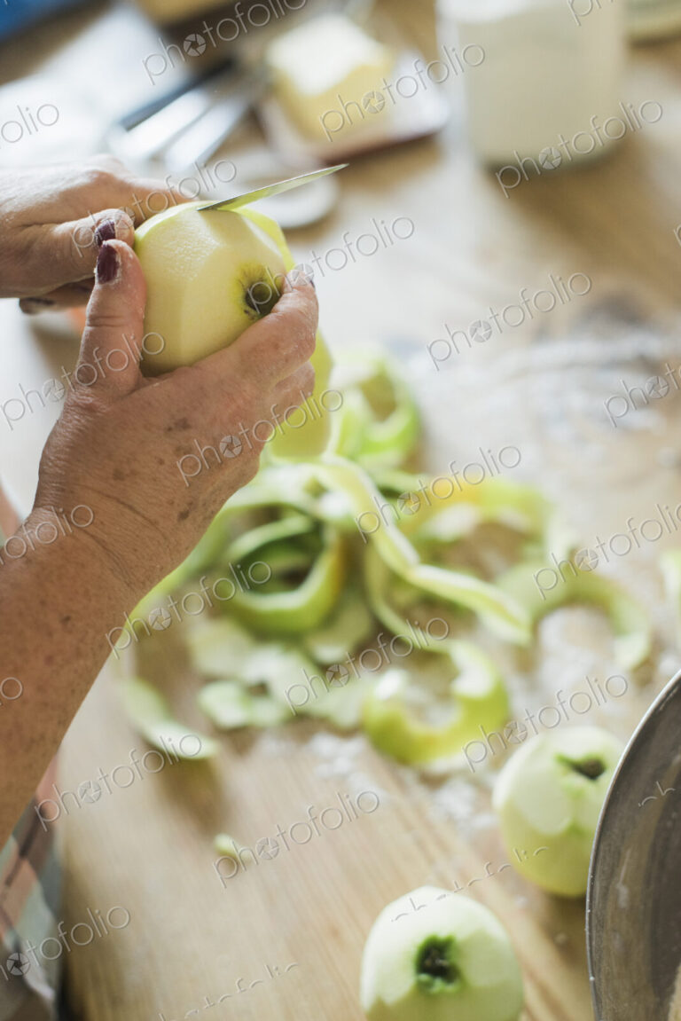 A woman peeling a green skinned apple.