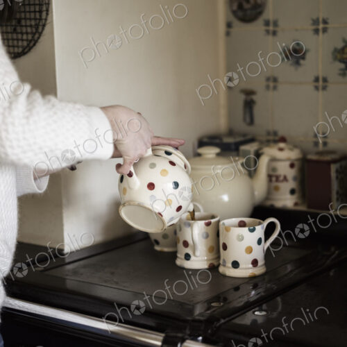 A woman pouring tea, by a range cooker. Using decorative china. A woman pouring tea, by a range cooker. Using decorative china.