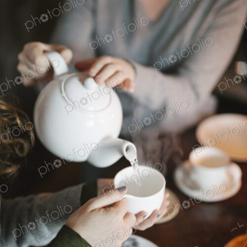 A woman pouring tea from a teapot into a cup for a companion. A woman pouring tea from a teapot into a cup for a companion.