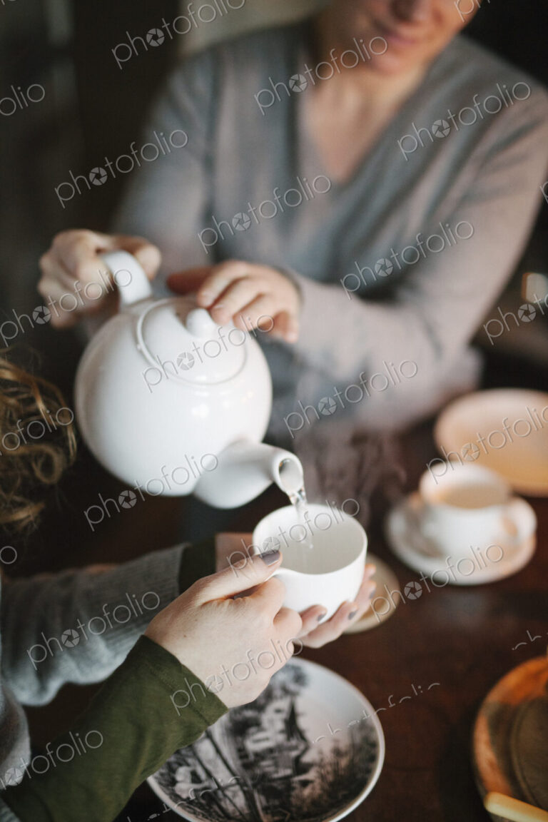 A woman pouring tea from a teapot into a cup for a companion.