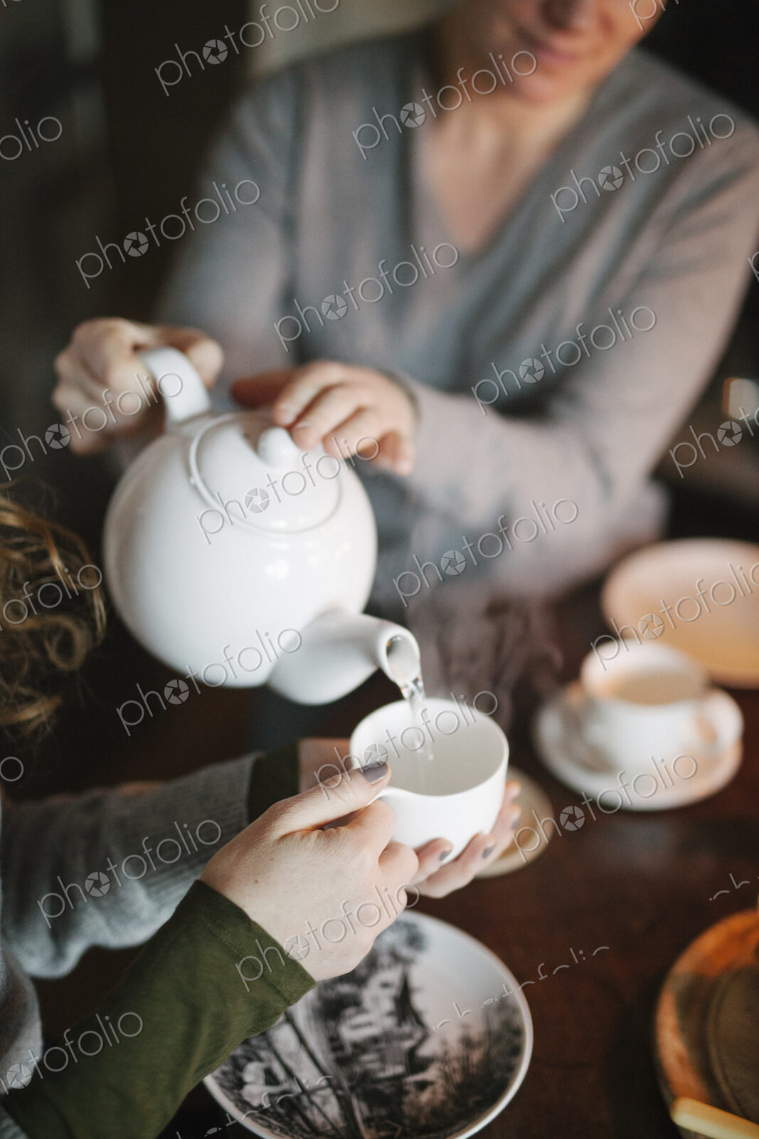 A woman pouring tea from a teapot into a cup for a companion.