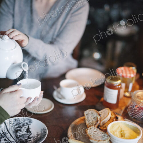 A woman pouring tea from a teapot into a cup for a companion. A woman pouring tea from a teapot into a cup for a companion.