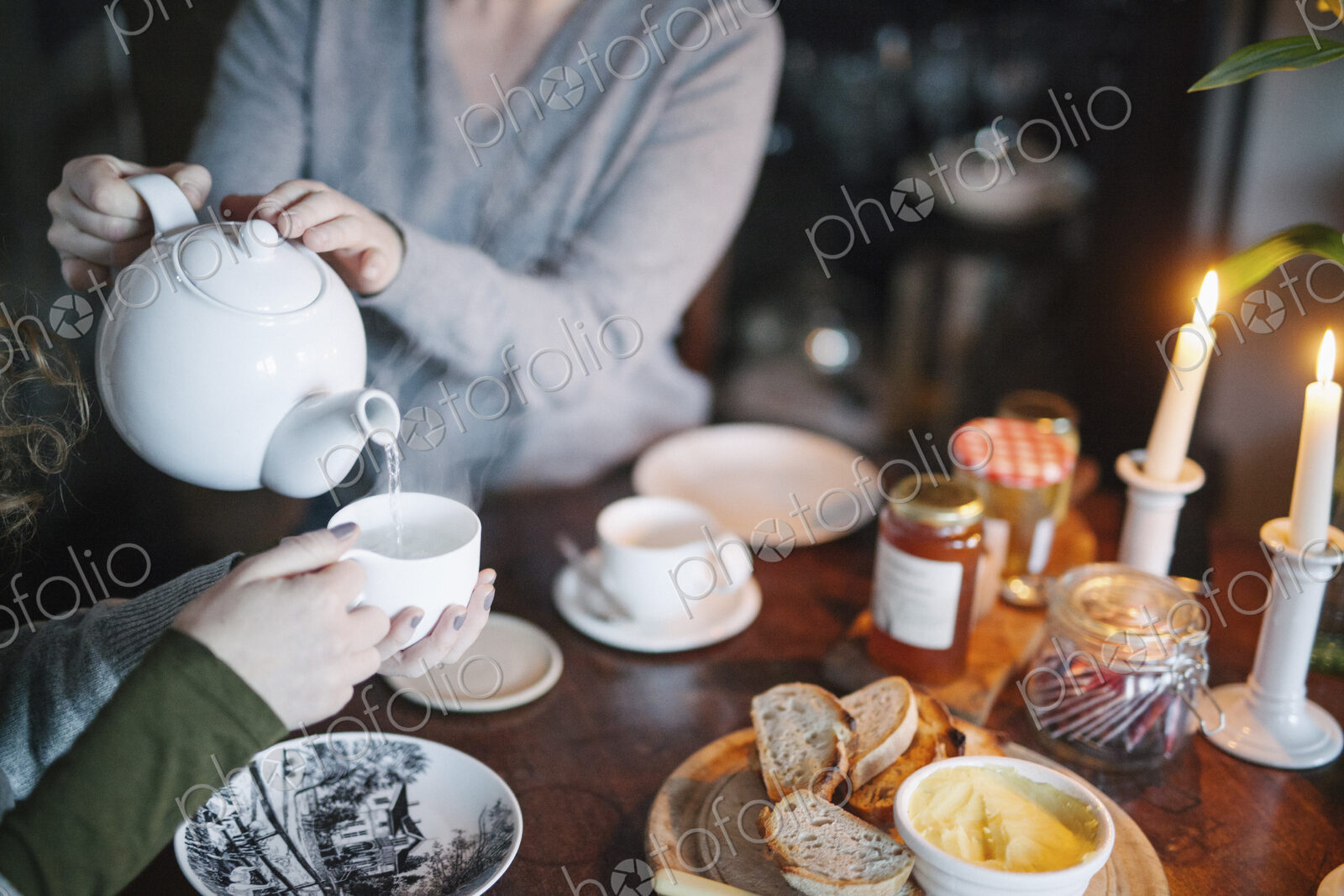A woman pouring tea from a teapot into a cup for a companion.