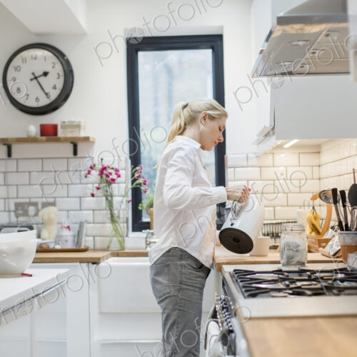 A woman pouring water from a kettle into a mug in a modern kitchen. A woman pouring water from a kettle into a mug in a modern kitchen.
