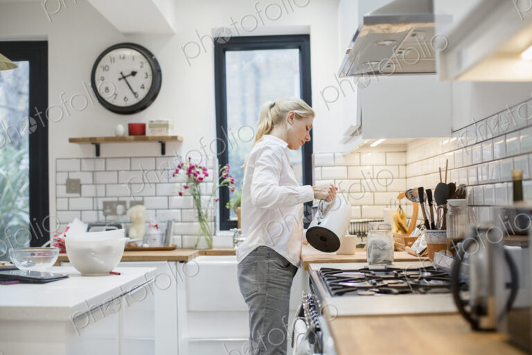 A woman pouring water from a kettle into a mug in a modern kitchen.