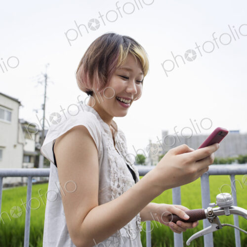 A woman pushing a bicycle while looking at her cell phone.