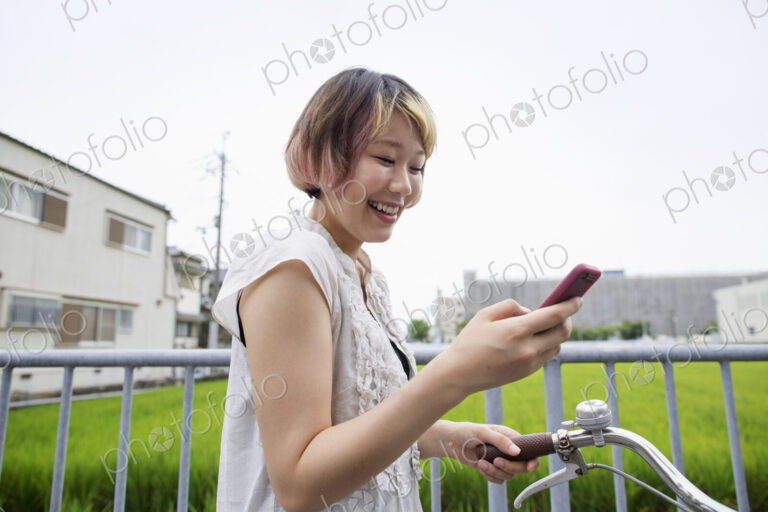 A woman pushing a bicycle while looking at her cell phone.