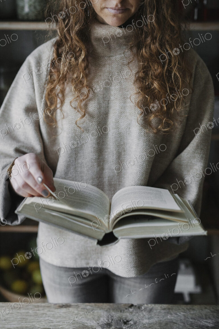 A woman reading from a recipe book in a kitchen.