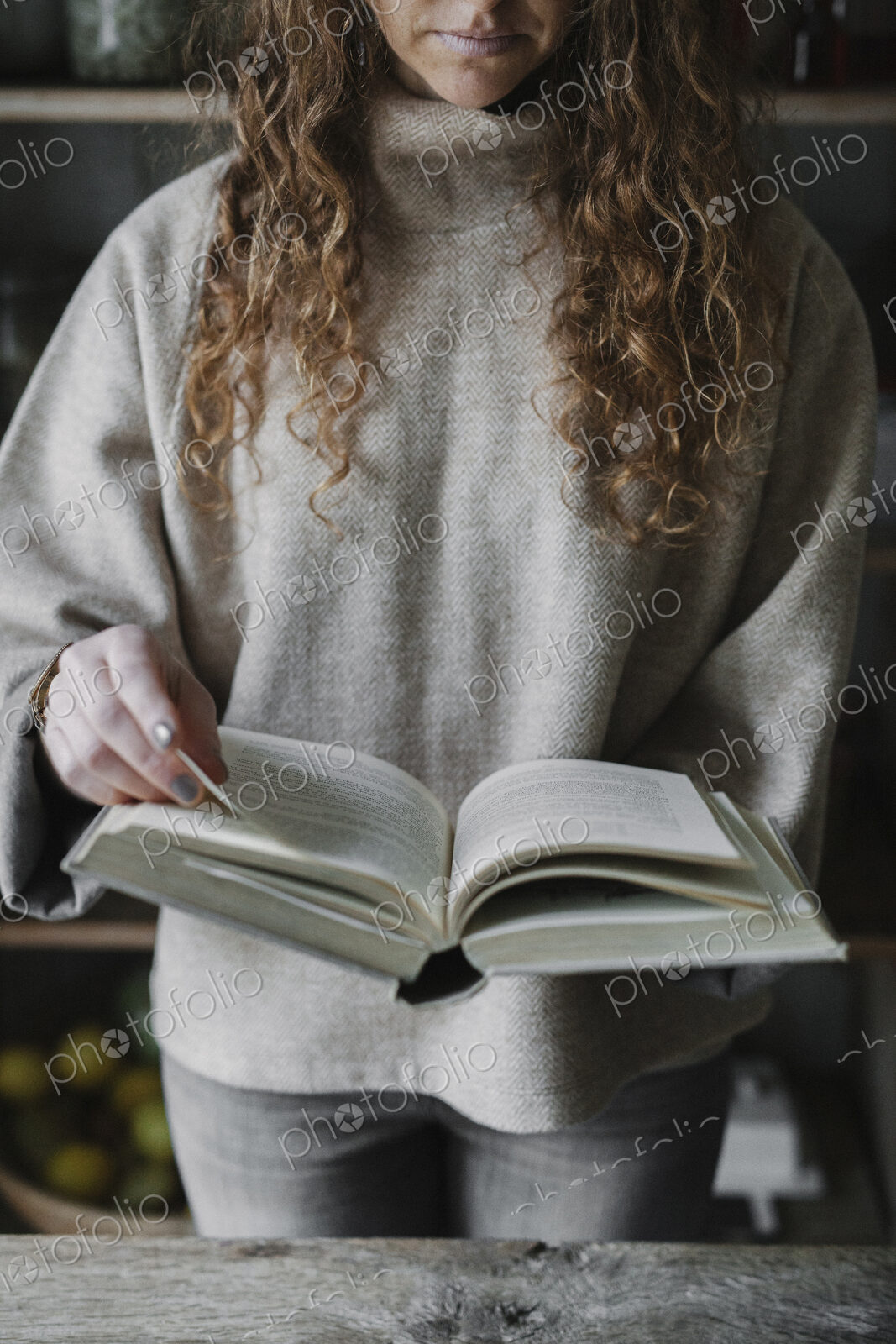 A woman reading from a recipe book in a kitchen.