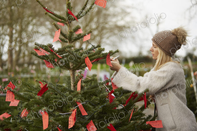 A woman reading handwritten red labels tied to the branches of a Christmas tree.