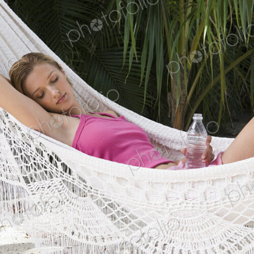 A woman relaxing in a hammock holding a bottle of water. A woman relaxing in a hammock holding a bottle of water.