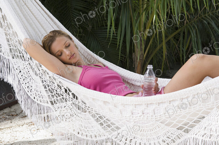 A woman relaxing in a hammock holding a bottle of water.