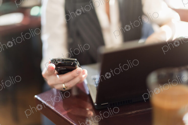 A woman seated at a desk holding a smart phone, with a laptop computer.