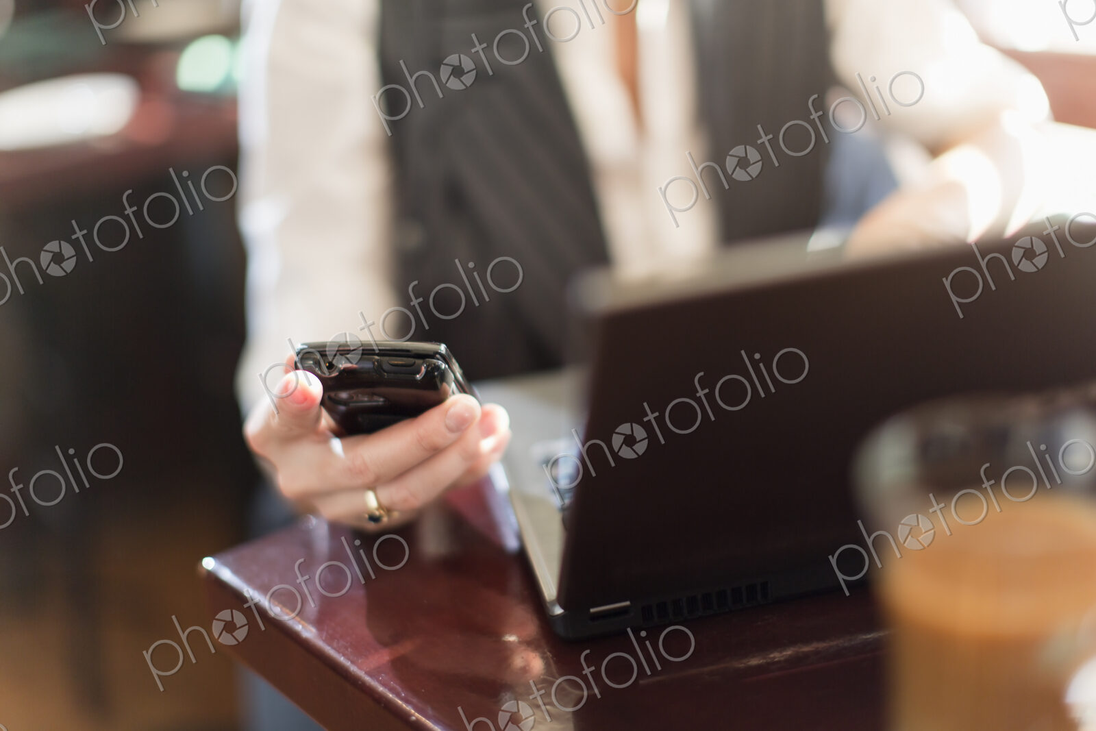 A woman seated at a desk holding a smart phone, with a laptop computer.