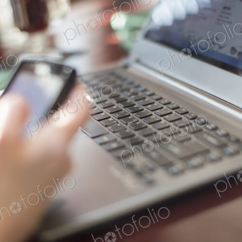 A woman seated at a desk holding a smart phone, with a laptop computer.