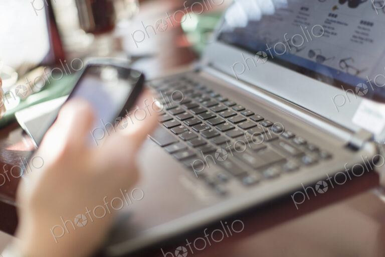 A woman seated at a desk holding a smart phone, with a laptop computer.