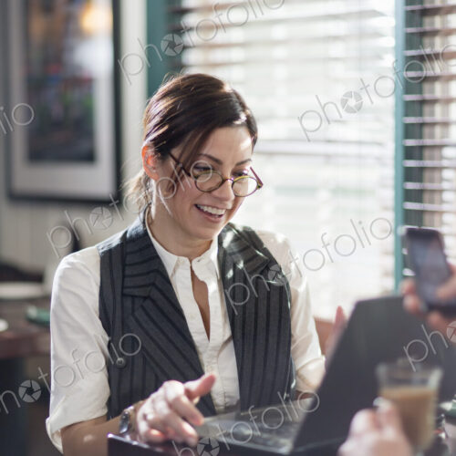 A woman seated at a desk, working over lunch. Using a laptop and mobile.