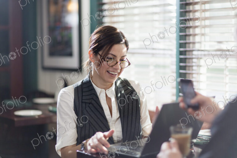 A woman seated at a desk, working over lunch. Using a laptop and mobile.