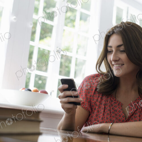 A woman seated at a table, checking her smart phone. A woman seated at a table, checking her smart phone.