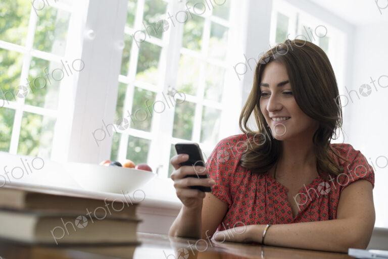 A woman seated at a table, checking her smart phone.