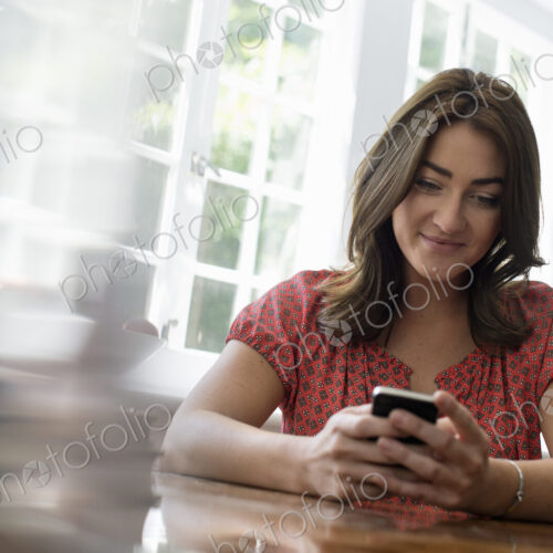A woman seated at a table, checking her smart phone. A woman seated at a table, checking her smart phone.