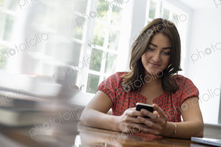 A woman seated at a table, checking her smart phone.