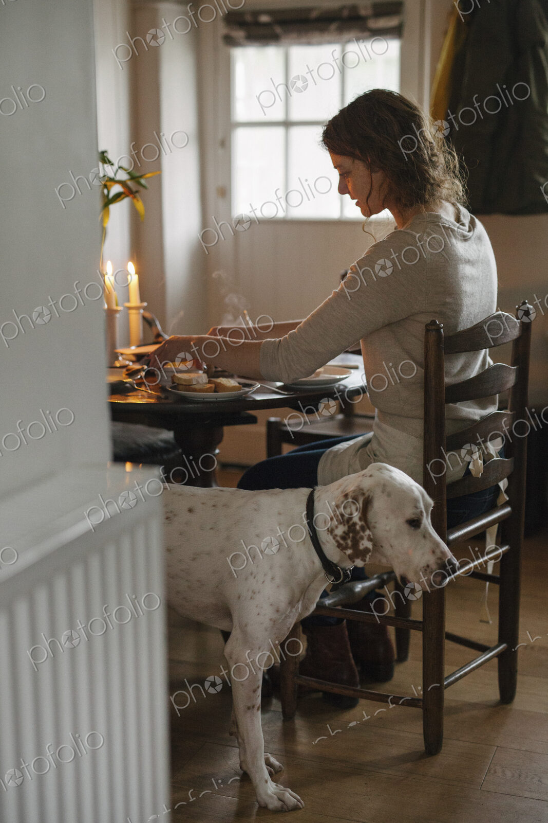 A woman seated at a table in a ladderback chiar, a large white dog beside her.