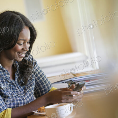A woman seated at a table with a cup of coffee, using a smart phone. A woman seated at a table with a cup of coffee, using a smart phone.
