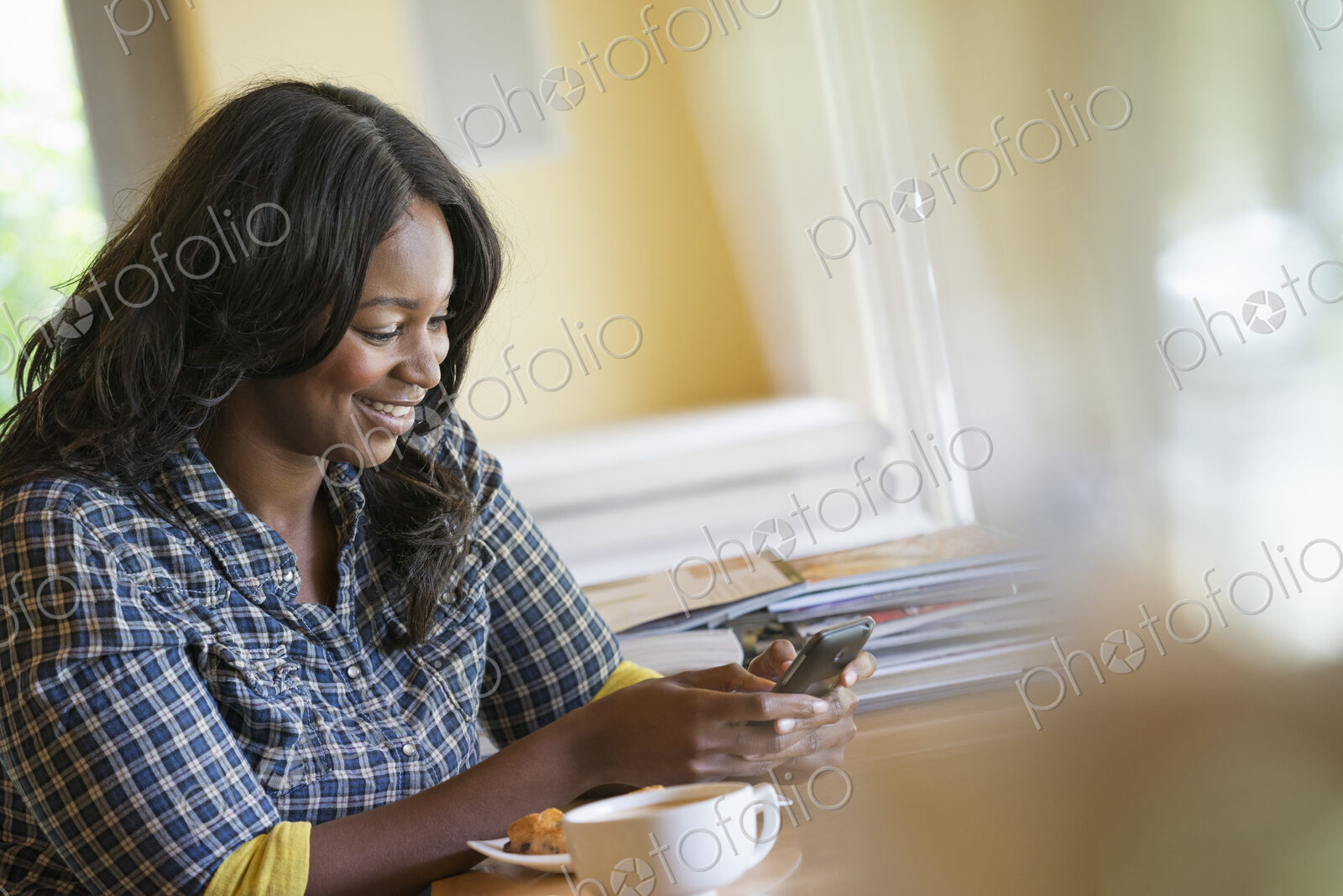 A woman seated at a table with a cup of coffee, using a smart phone.