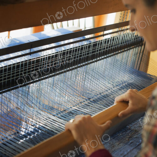A woman seated at a wooden handloom creating a handwoven woollen fabric, with a blue… A woman seated at a wooden handloom creating a handwoven woollen fabric, with a blue…