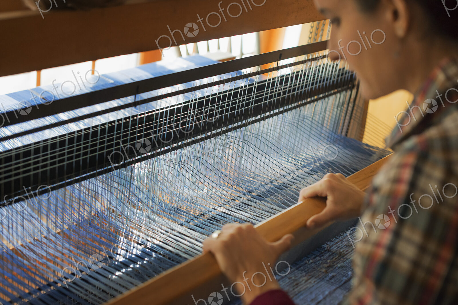 A woman seated at a wooden handloom creating a handwoven woollen fabric, with a blue…