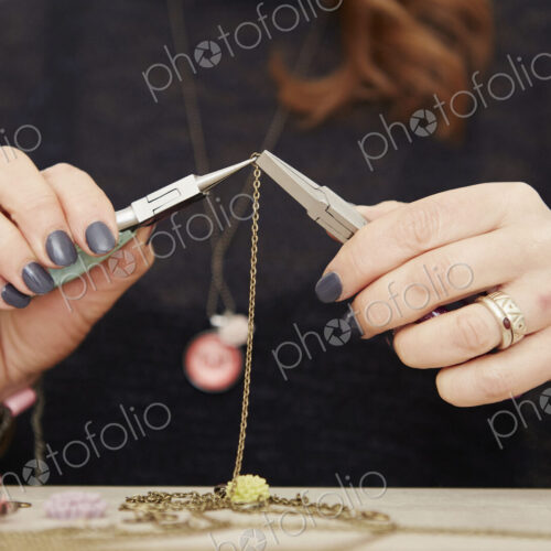 A woman seated at a workbench holding a gold chain, making jewellery.