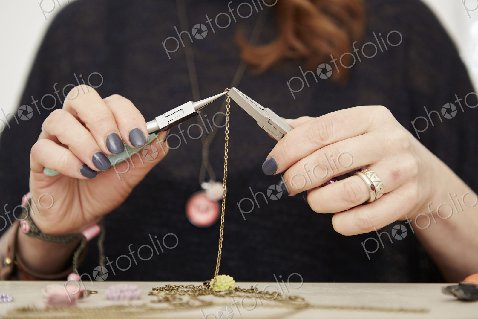 A woman seated at a workbench holding a gold chain, making jewellery.