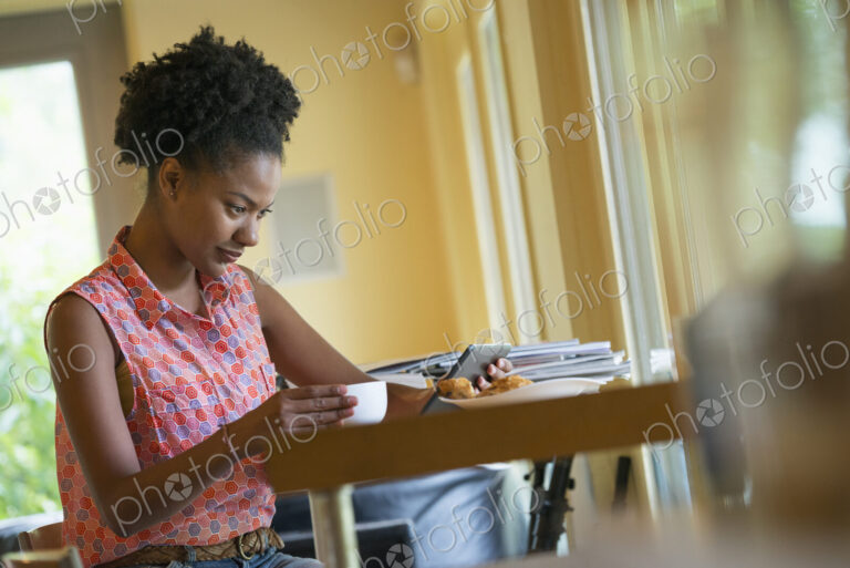 A woman seated having a cup of coffee. Holding an ebook or a digital tablet.