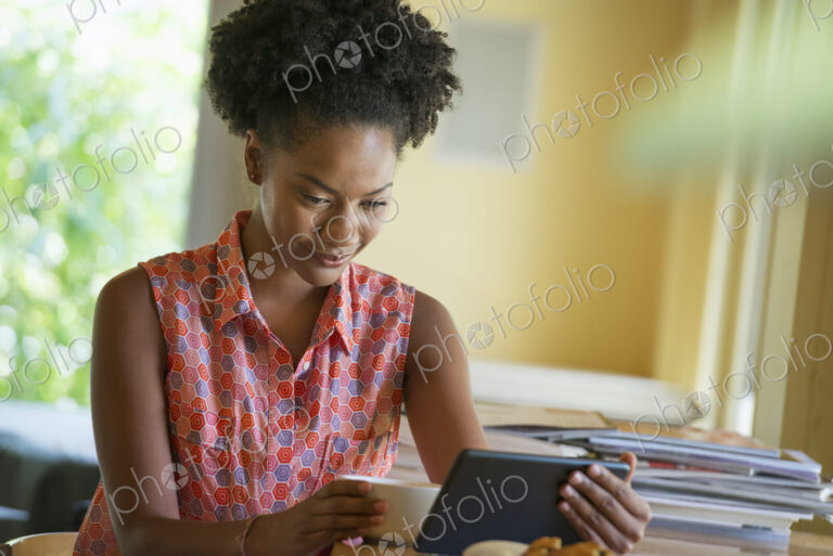 A woman seated having a cup of coffee. Holding an ebook or a digital tablet.