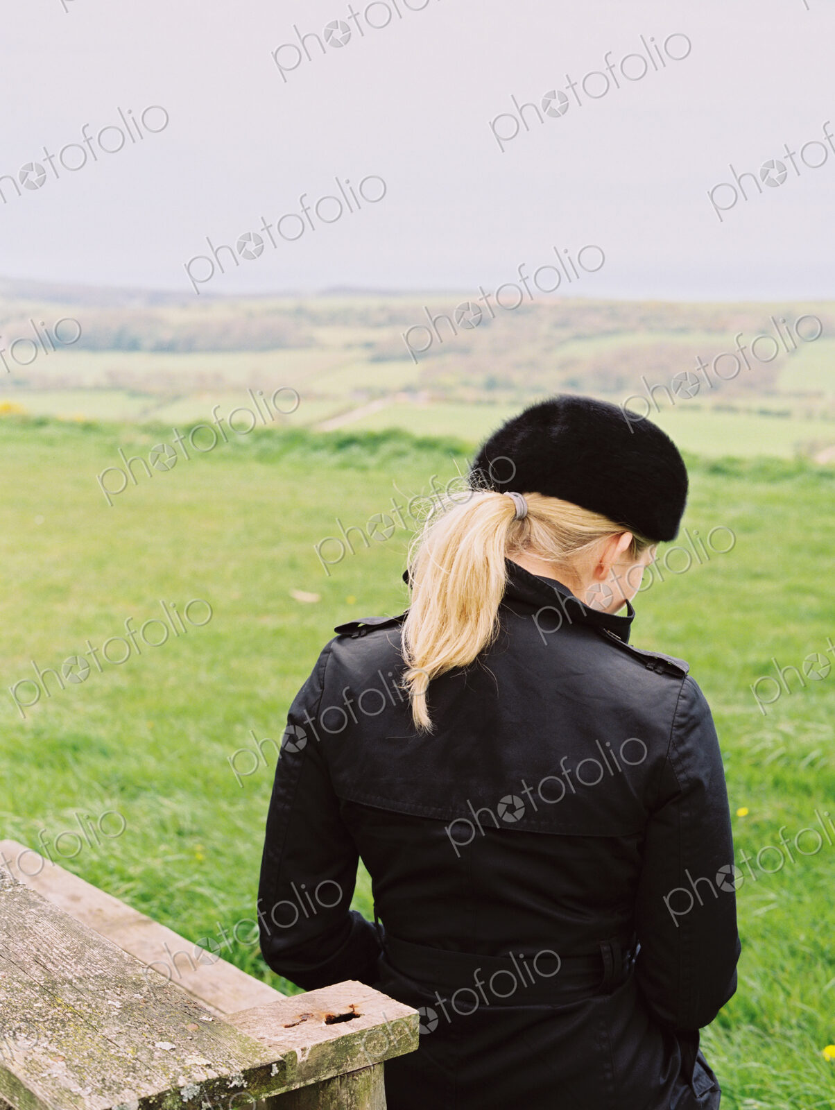 A woman seated on a bench looking over the landscape to the sea.