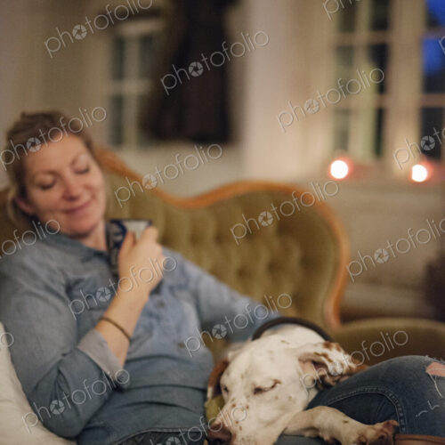 A woman seated on a sofa with a large dop with his head on her lap. A woman seated on a sofa with a large dop with his head on her lap.