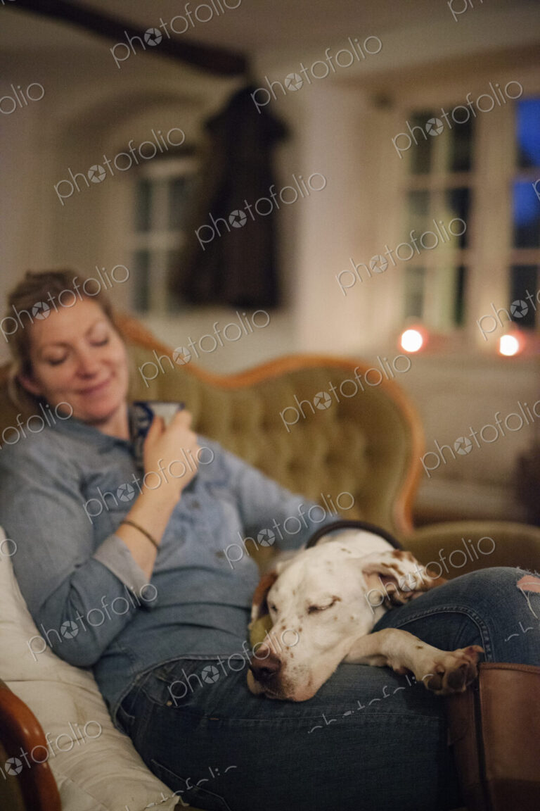 A woman seated on a sofa with a large dop with his head on her lap.