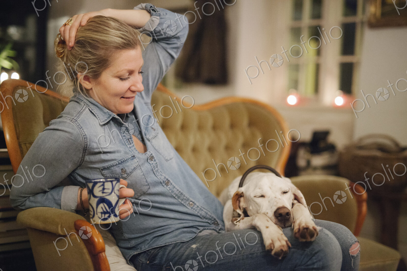 A woman seated on a sofa with a large dop with his head on her lap.