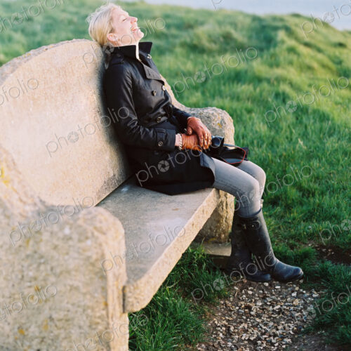 A woman seated on a stone bench on a coastal path. A woman seated on a stone bench on a coastal path.