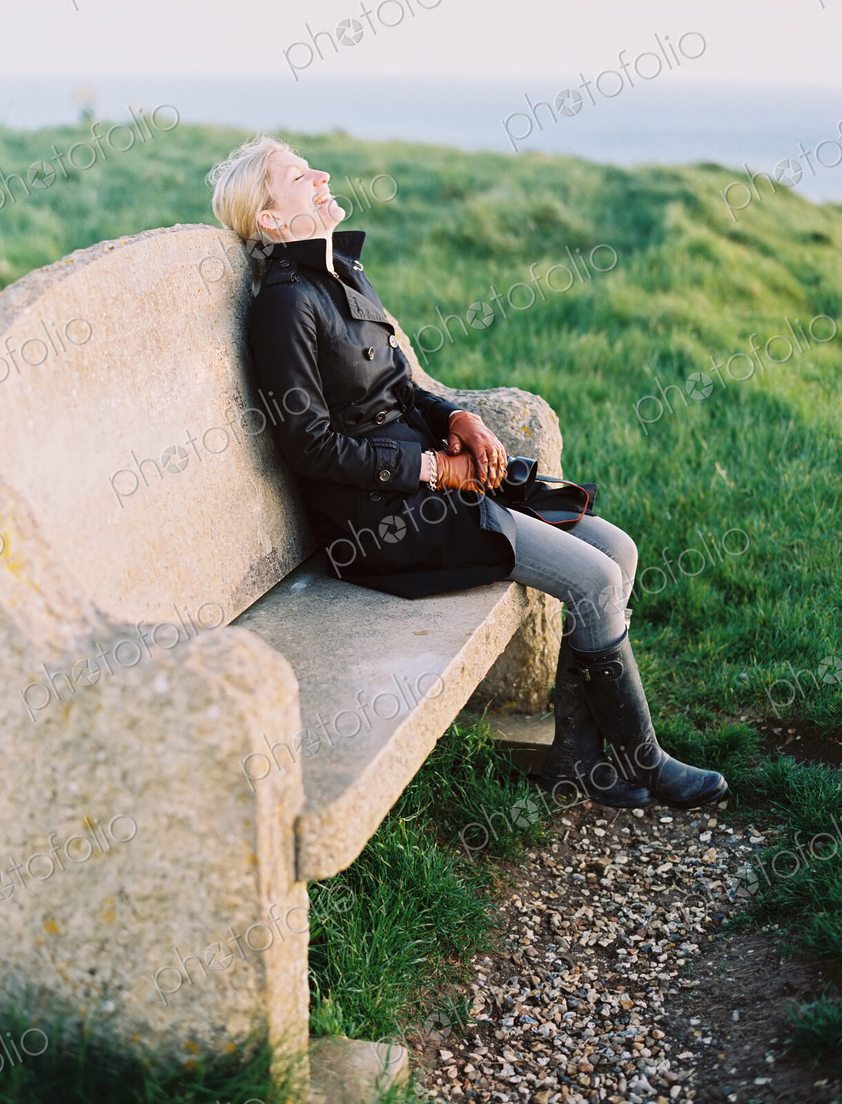 A woman seated on a stone bench on a coastal path.