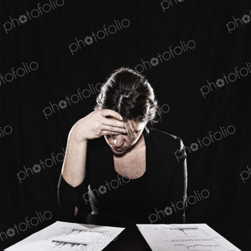 A woman seated with her hand on her forehead, reading documents. Studio portrait. A woman seated with her hand on her forehead, reading documents. Studio portrait.