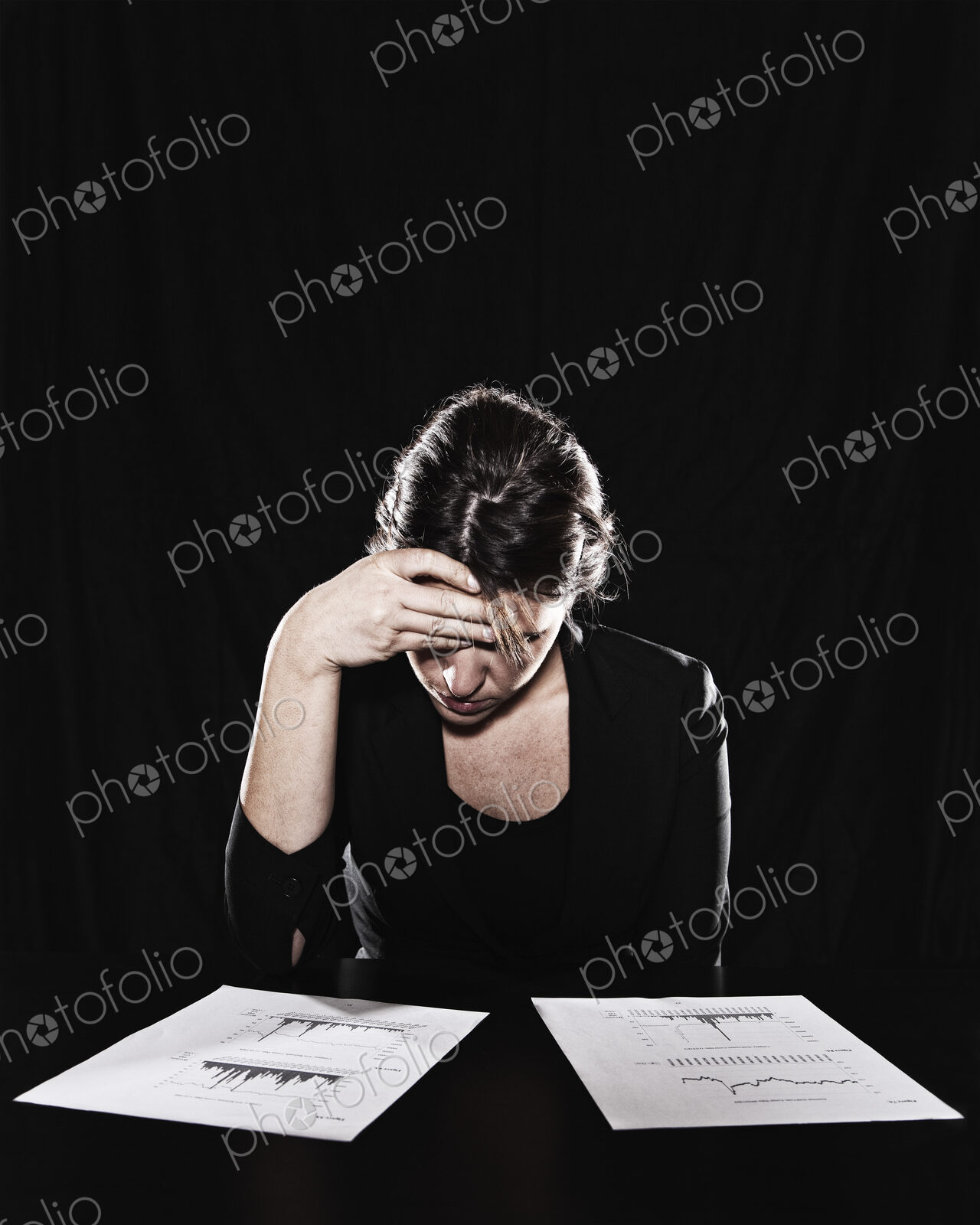 A woman seated with her hand on her forehead, reading documents. Studio portrait.