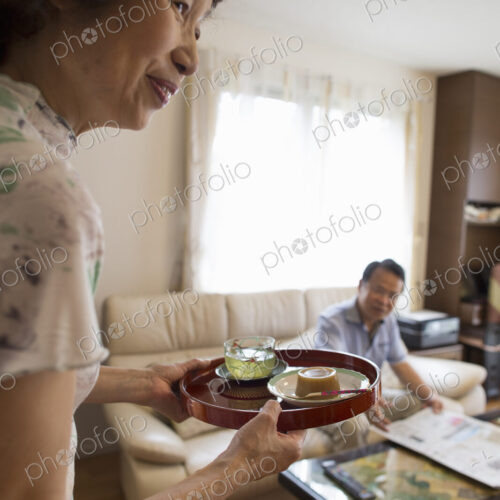 A woman serving a tray of food to a man sitting on a sofa.