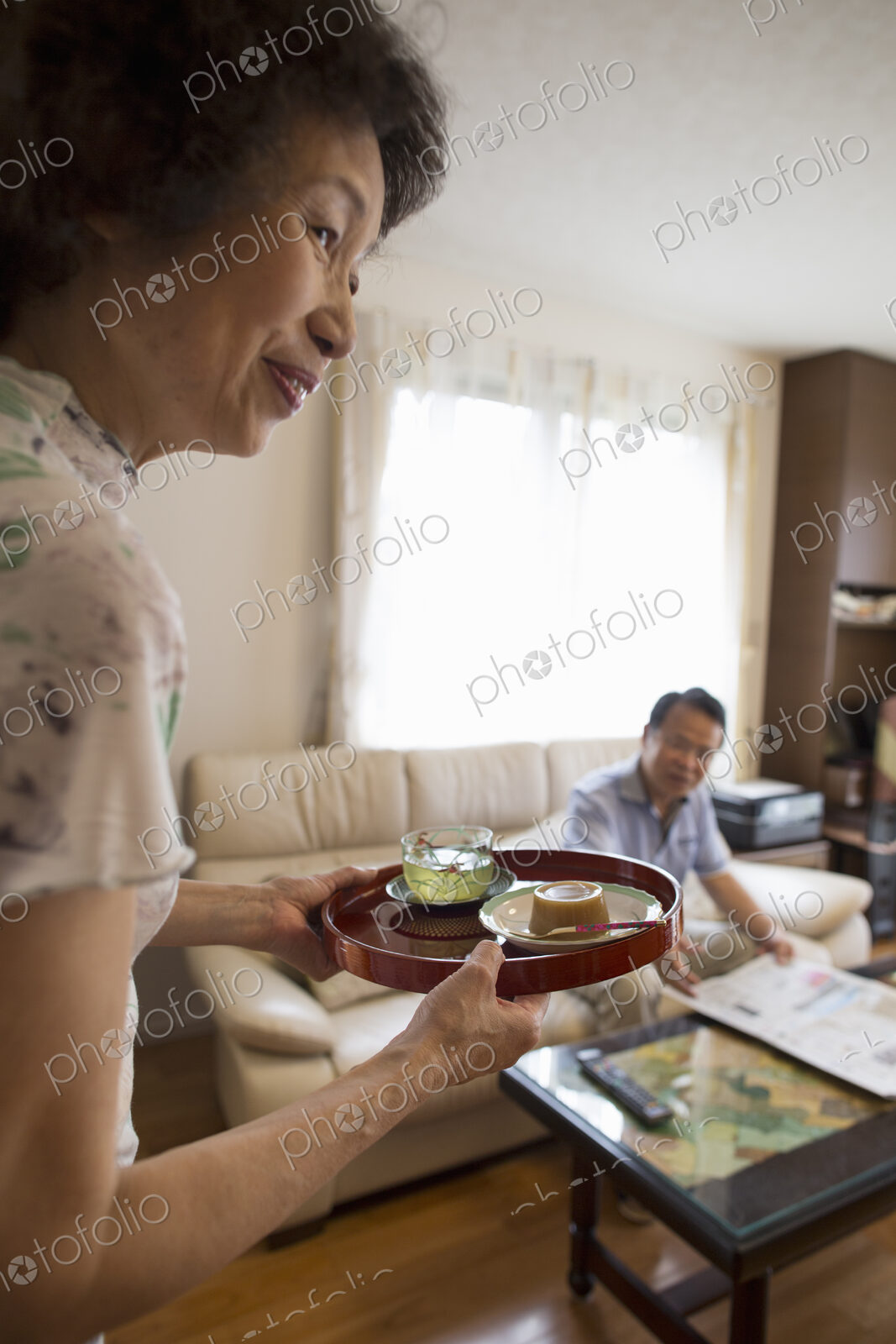A woman serving a tray of food to a man sitting on a sofa.