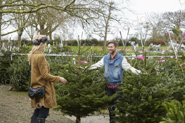 A woman shopping for a Christmas tree, assisted by staff.