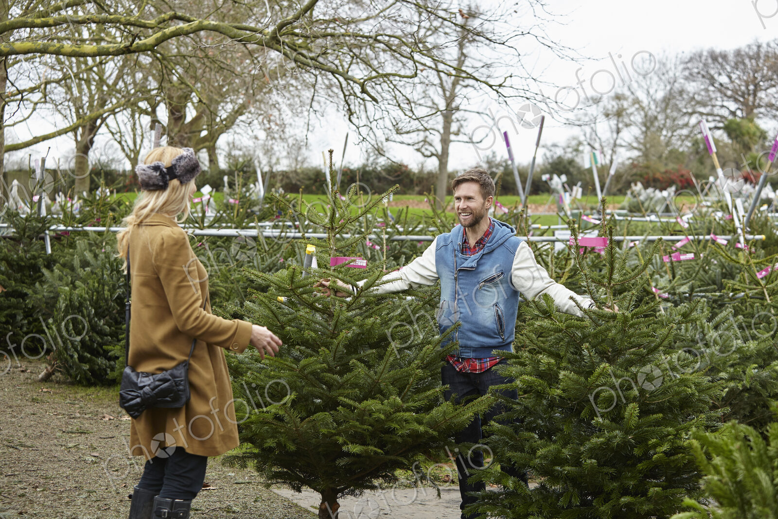 A woman shopping for a Christmas tree, assisted by staff.