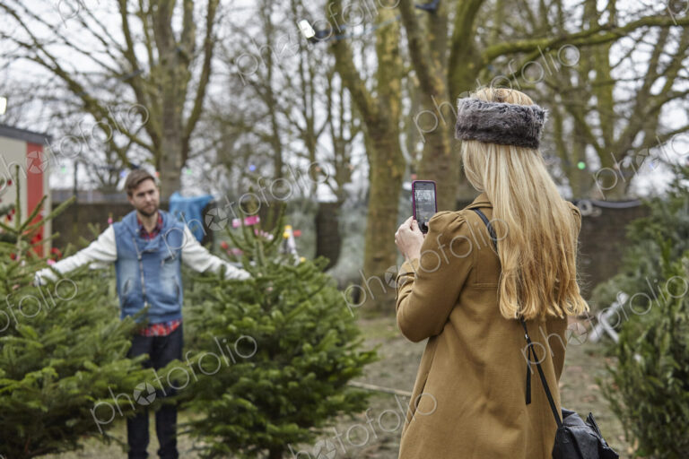 A woman shopping for a Christmas tree, assisted by staff.